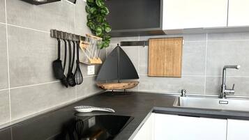 A modern kitchen with a black stove, a wooden cutting board, and a hanging utensil rack.