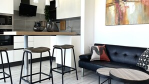 Ett modernt kök med barstolar, en svart soffa och en tavla.