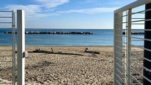 En strand med utsikt över havet, en brygga i bakgrunden och en vit grind.