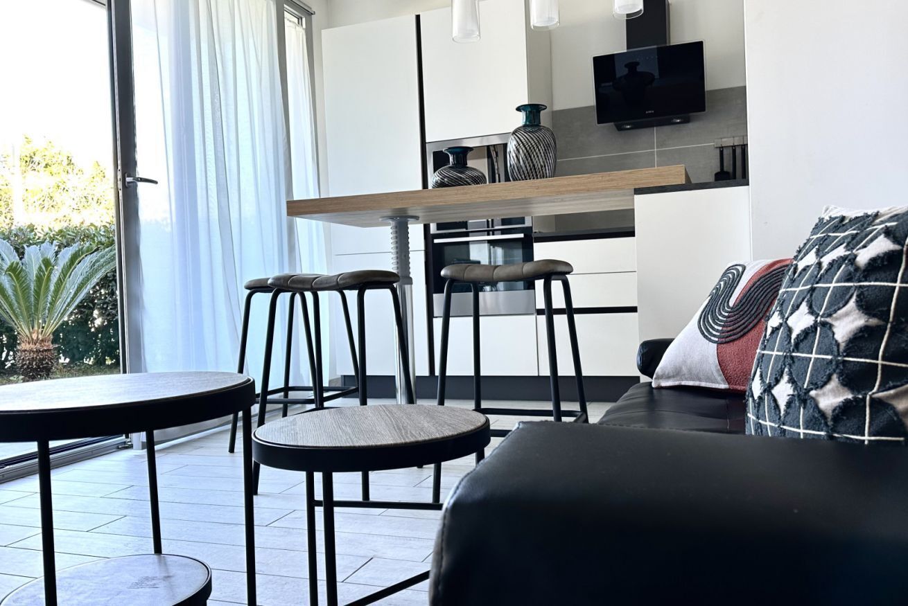A modern kitchen with a flat-screen TV, a dining area with stools, and a sofa with patterned cushions.