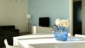 A dining table with a vase of flowers, a television, and a lamp in a room with a light blue wall. - M379 - Marcelli, renovated three-room apartment with terrace overlooking the sea (Marcelli)