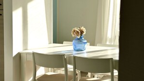 A dining table with chairs, a blue vase with dried flowers, and sunlight streaming through a window. - M379 - Marcelli, renovated three-room apartment with terrace overlooking the sea (Marcelli)