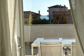 A balcony with a table and chairs, overlooking a residential area with buildings and a clear sky.