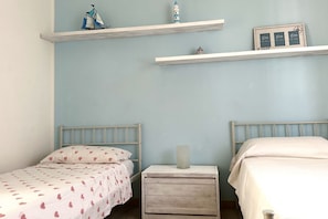 A bedroom with two beds, a nightstand, and shelves with decorative items.