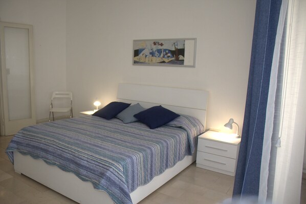 A bedroom with a bed, bedside tables, a nightstand, and a painting on the wall.