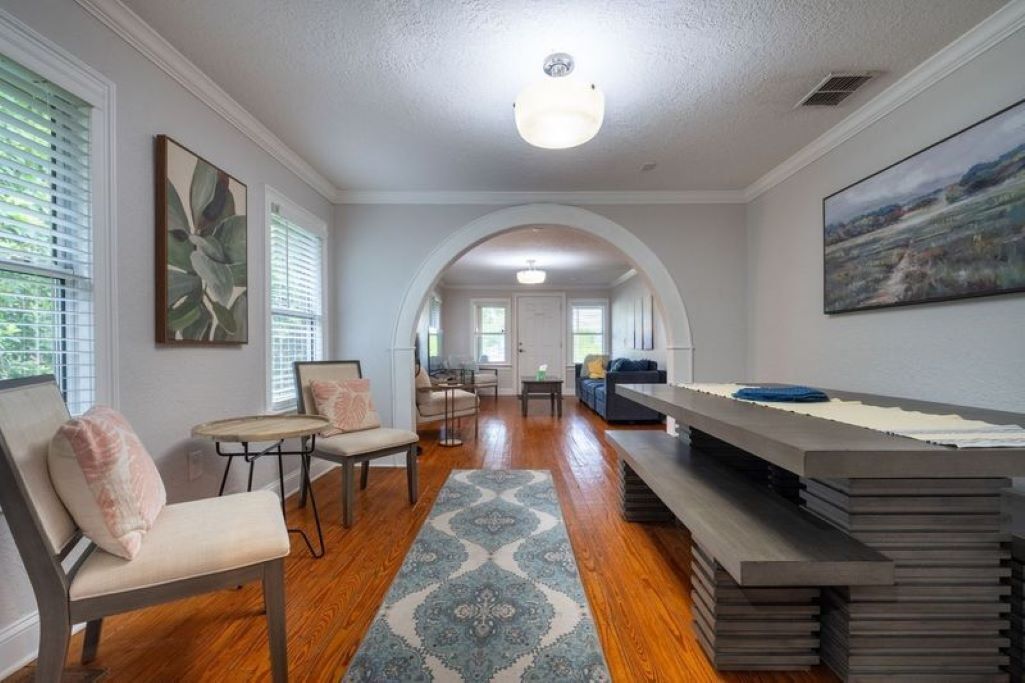 A spacious living room with hardwood floors, a patterned rug, and a long dining table.