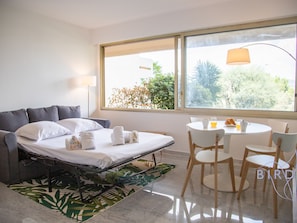 Relax in a serene space with a comfortable bed, a cozy sofa, and a view of lush greenery outside.
