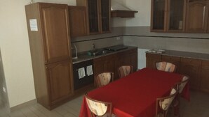 Een compacte keuken met houten kastjes, een inbouwfornuis en een eettafel met stoelen.