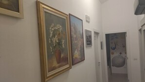 Een gang met ingelijste kunstwerken aan de muur, een deur met een kleurrijke muurschildering, en een vloerkleed met een patroon.