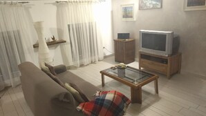 Een woonkamer met een bank, een salontafel, een televisie op een houten standaard en een witte muur met twee foto's in lijsten.