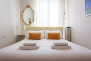 Une chambre d’hôtel avec un lit, deux oreillers, une table de chevet avec une lampe, un miroir et un radiateur.