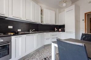 A modern kitchen with white cabinets, a black countertop, and a dining area with a chair and table.