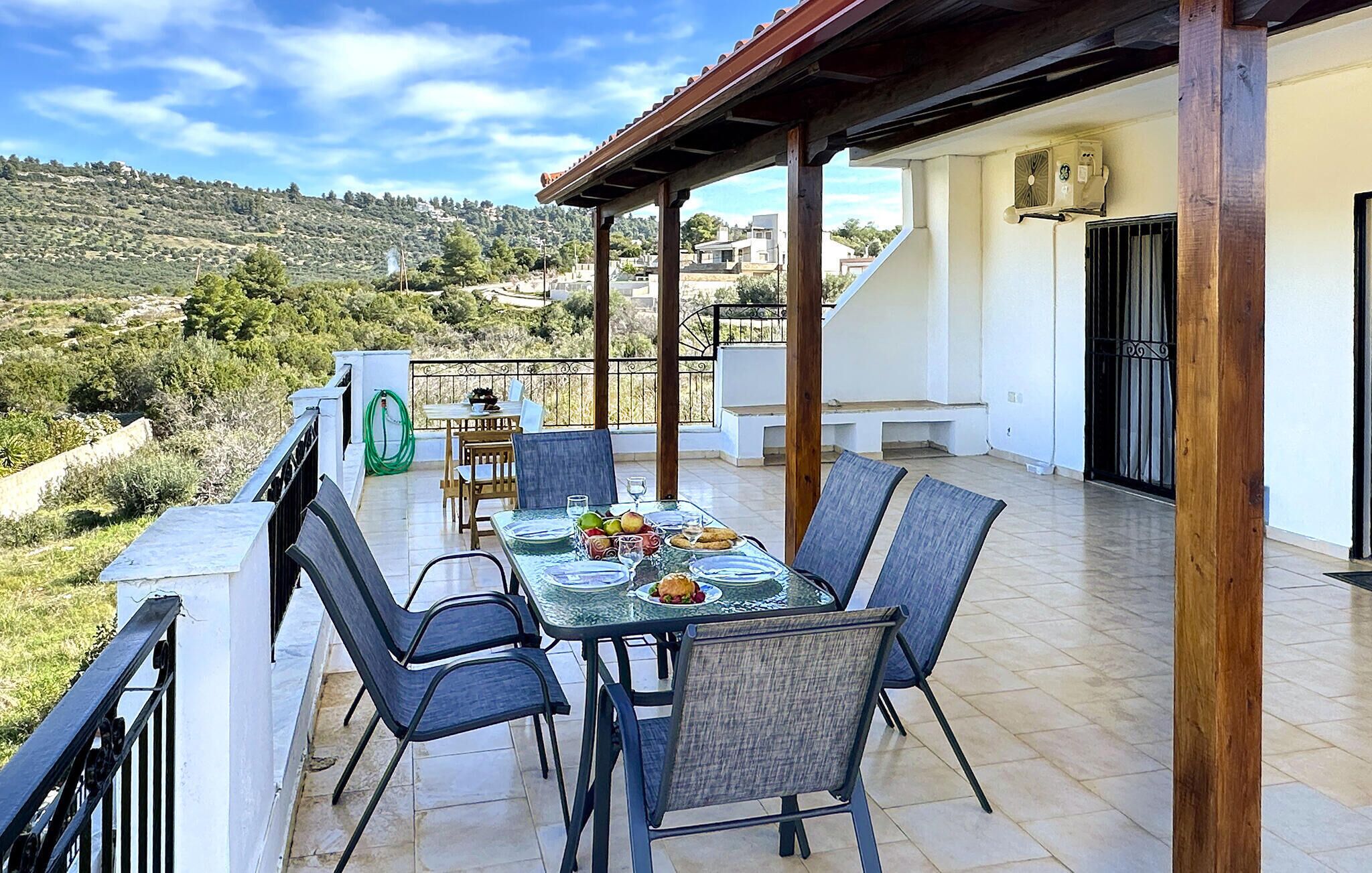 Una terraza con mesa lista para comer, rodeada de sillas y vistas a una ladera pintoresca.