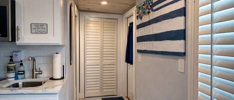 A hallway with a kitchen area on the left, a door with a sign, and a wall with a striped pattern.