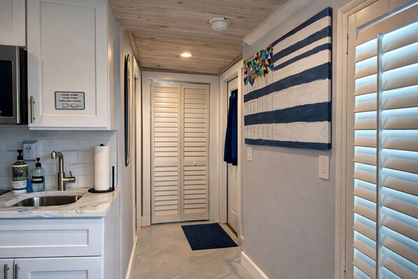 A hallway with a kitchen area on the left, a door with a sign, and a wall with a striped pattern.