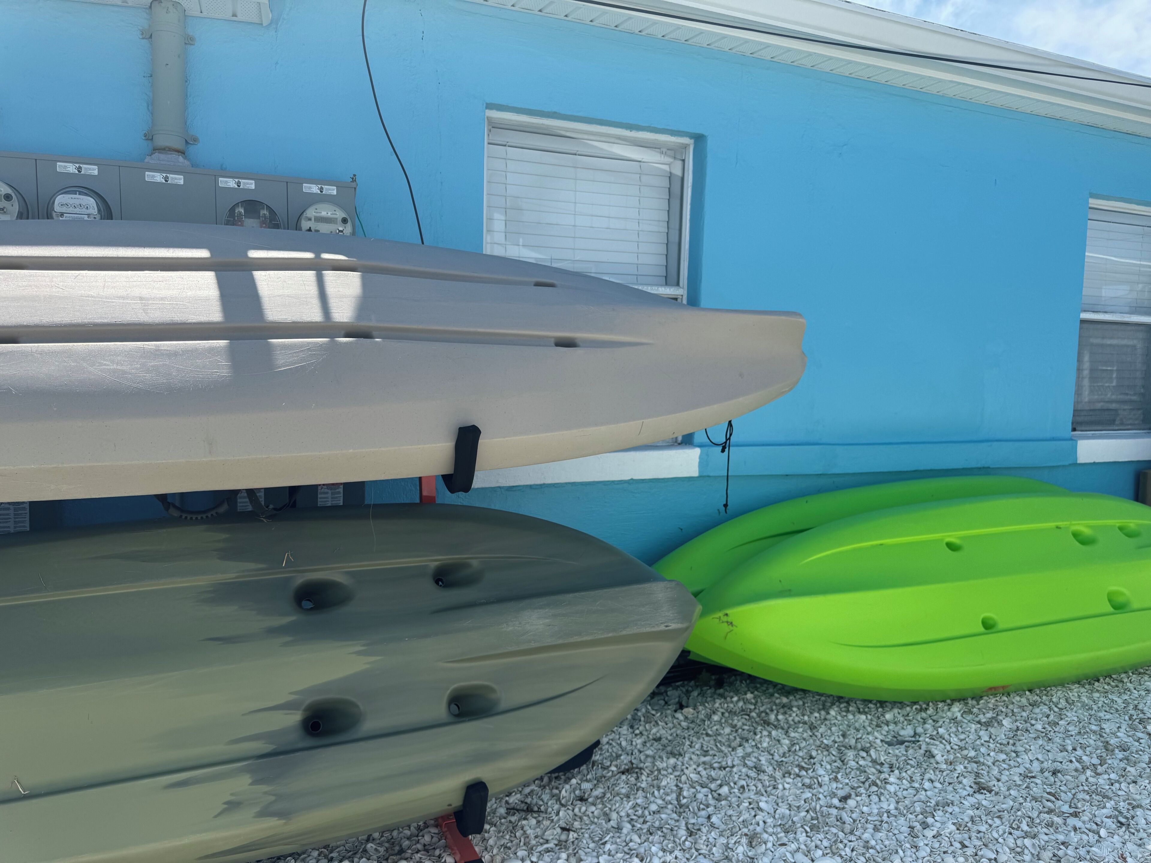 A kayak and a canoe parked against a building with a window and a door.