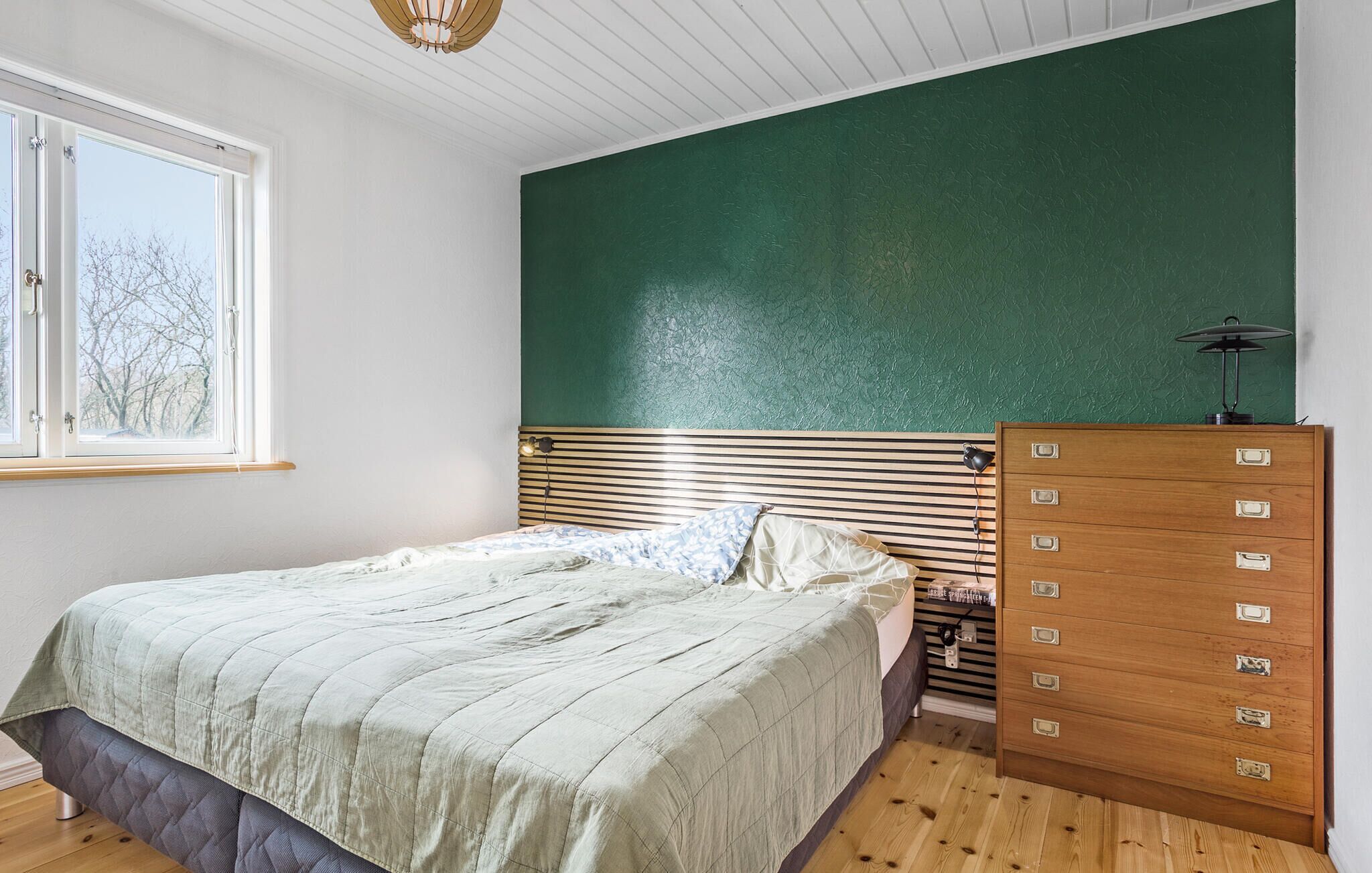 A bedroom with a bed, a dresser, a window, and a green accent wall.