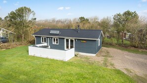 Una pequeña casa de un piso con techo oscuro, un porche delantero y una chimenea visible.