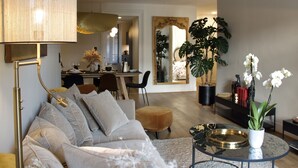 A modern living room with a sofa, a coffee table, and a lamp. There is a dining area in the background with a table and chairs.