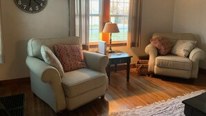 A living room with two armchairs, a side table, a lamp, and a wall clock. - Cozy and relaxing (Linton)