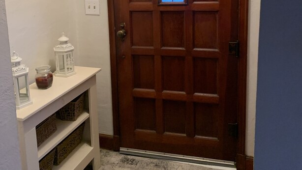 A wooden door with a window, a white shelf with jars and lanterns, and a white wall with a light switch. - Cozy and relaxing (Linton)