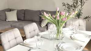 Une table à manger dressée avec de l’argenterie blanche, des verres et des couverts, entourée de chaises à revêtement gris.
