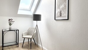 Une pièce moderne avec une lucarne, un tableau encadré, un lampadaire et une chaise.