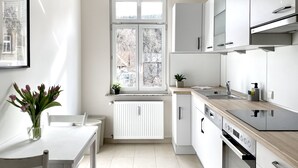 Une cuisine moderne avec des meubles blancs, un four encastré et une fenêtre donnant sur les arbres.