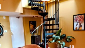 Un amplio salón con una escalera moderna, un sillón cómodo, una mesita de centro y una planta en maceta.