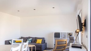 En moderne stue med en grå sofa, hvide stole, et lille bord og et fjernsyn på et stativ.
