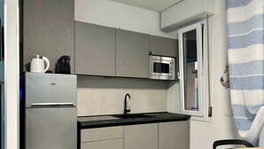 Eine kompakte Küche mit integriertem Kühlschrank, Mikrowelle und Spüle, ausgestattet mit grauen Schränken und einer schwarzen Arbeitsplatte.