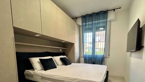 Ein Schlafzimmer mit einem Bett, einem an der Wand befestigten Fernseher und einem Fenster mit Vorhängen.