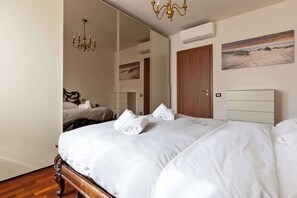 Une chambre à coucher avec un grand lit, une tête de lit en bois, un lustre, un grand miroir, un tableau et une porte.