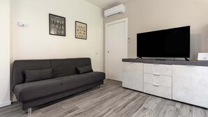 En moderne stue med en grå sofa, et fladskærms-tv og et hvidt skab.