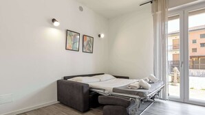 Ett modernt sovrum med en bäddsoffa, en liten sittgrupp och ett stort fönster med utsikt över omgivningen.