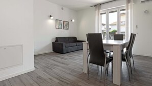 Ett modernt vardagsrum med en grå soffa, ett matbord med fyra stolar och ett stort fönster med gardiner.