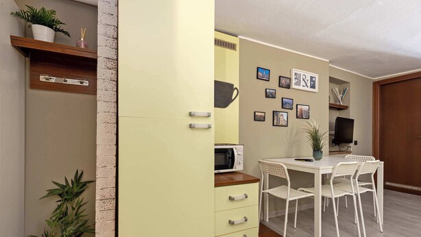 Ett kompakt bostadsutrymme med ett litet kök, en matplats med bord och stolar samt en vägg som är dekorerad med inramade bilder.