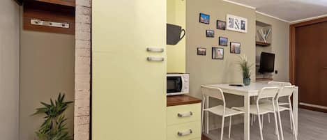 A compact living space with a kitchenette, a dining area with a table and chairs, and a wall adorned with framed pictures.