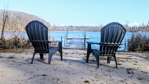 Kaksi Adirondack-tyylistä puutarhatuolia, jotka on asetettu vastakkain järven ääreen. Taustalla näkyy laituri ja laiturissa oleva vene.