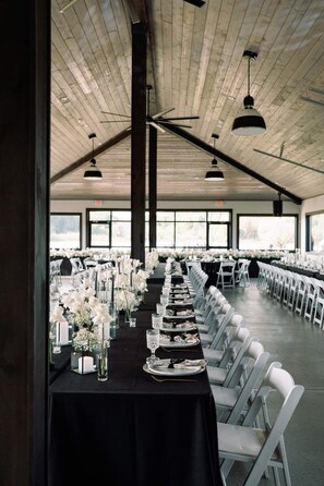 A long banquet table set for a formal event with white chairs, black tablecloths, and floral centerpieces.