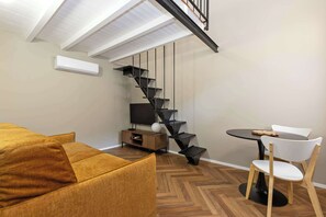 A modern living room with a sofa, a TV, a wooden dining table with chairs, and a unique black spiral staircase. - Civico 13 - Immobili e Soluzioni Rent (Bergamo)