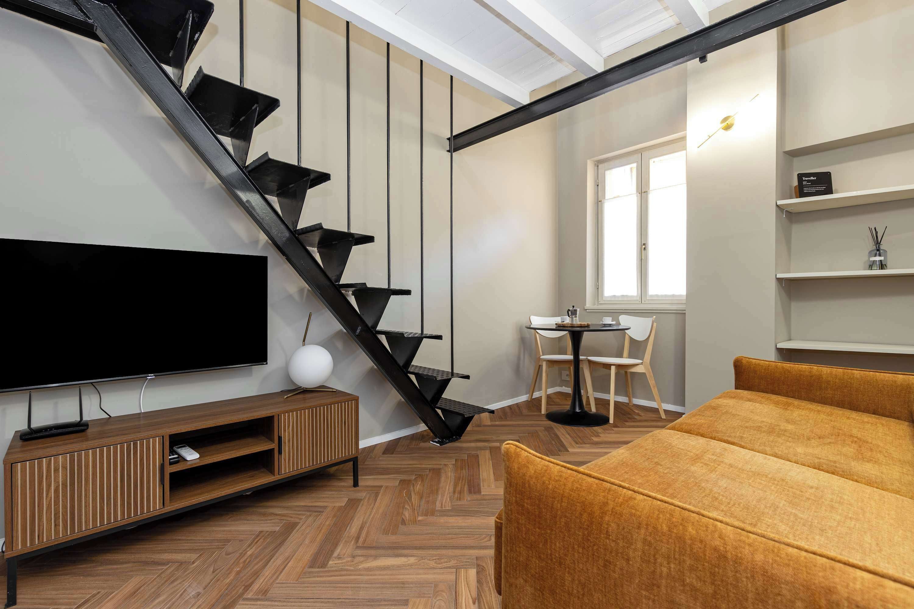 Una sala de estar moderna con una escalera espiral negra, un televisor de pantalla plana, un mueble de entretenimiento de madera, una mesa de centro redonda y un sofá.