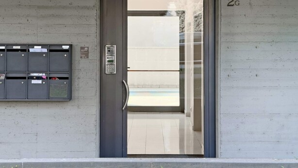 Una puerta moderna con cerradura electrónica, un buzón con ranuras para correo y el número '2G' en la pared.