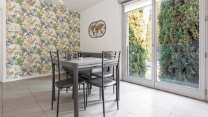 Un comedor con una mesa y sillas, un mapa mural del mundo y vistas a un seto verde a través de una puerta de vidrio.
