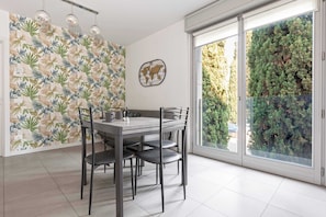 A dining area with a table and chairs, a world map wall decoration, and a view of a green hedge through a glass door.