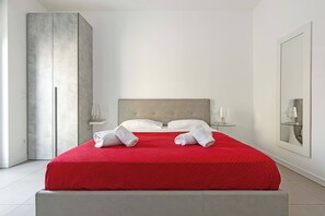 A modern hotel room with a large bed, a grey headboard, white walls, and a large mirror.