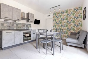 A modern kitchen with grey cabinets, a tiled backsplash, and a dining area with a grey sofa and table.