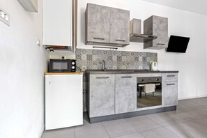 A modern kitchen with grey cabinets, a white refrigerator, a microwave, and a tiled backsplash. - Vivaldi Home - Immobili e Soluzioni Rent (Bergamo)