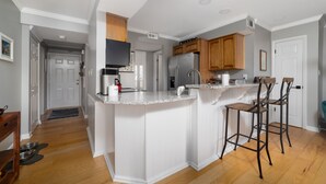 A kitchen with white cabinetry, a granite countertop, a stainless steel refrigerator, and two bar stools. - Quaint and Cozy Lake Norman Condo Lakefront Walkable Dogs Ok (Davidson)