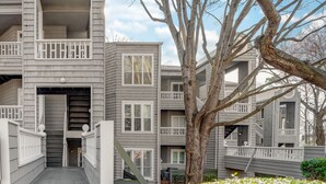 A multi-story residential building with a central staircase, balconies, and a large tree in the foreground. - Quaint and Cozy Lake Norman Condo Lakefront Walkable Dogs Ok (Davidson)